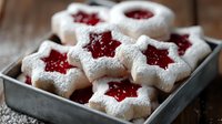 Star-shaped shortbread cookies with red jam centers dusted with powdered sugar on rustic wooden background, traditional holiday baking for festive celebrations.