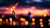 Wind turbine silhouette against dramatic sunset sky with glowing orange bokeh lights creating atmospheric mood for renewable energy and sustainability themes.