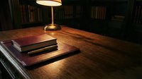 Wooden desk with stacked books and brass lamp in library setting, warm lighting for study, work, education, and professional office design projects.