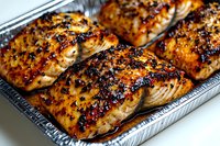 Grilled salmon fillets with caramelized glaze in aluminum tray ready for serving. Restaurant quality seafood dish with golden brown crust for culinary content.