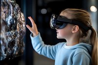 Young Caucasian girl wearing virtual reality headset reaches out to interact with digital display in museum or science center, expressing wonder and engagement.