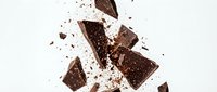 Chocolate pieces shattering and exploding in mid-air with cocoa powder dust cloud on white background, suitable for food and beverage advertising.