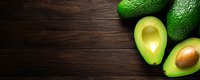 Fresh ripe avocados, whole and halved showing creamy flesh and pit on dark wooden background with copy space, banner composition for food design.