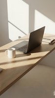 Modern minimalist workspace with laptop and coffee mug on wooden desk in natural sunlight for remote work and productivity concepts.