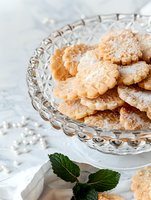 Homemade shortbread cookies dusted with powdered sugar served on vintage crystal plate with fresh mint leaves. Light marble background creates elegant mood.
