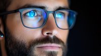 Close up portrait of young bearded man in glasses with blue light reflection in eyes and lenses, showing digital screen effect and modern technology impact.