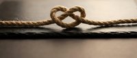 Natural jute rope tied in heart shape knot on wooden surface symbolizing love, unity and connection for romantic designs and wedding concepts.