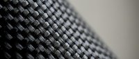 Black carbon fiber weave texture with detailed interlaced pattern showing industrial material surface for automotive and aerospace applications.