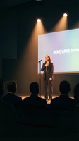 Professional businesswoman presenting innovation keynote speech on stage with microphone to corporate audience under dramatic spotlights.
