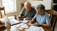 Senior Caucasian couple managing finances together at home, reviewing documents and using laptop for online banking and retirement planning.