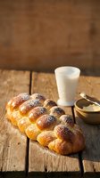 Fresh braided challah bread with sesame seeds on rustic wooden table with milk glass and honey bowl for traditional Jewish Shabbat celebration.