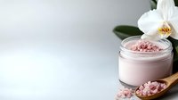 Pink Himalayan salt and orchid flower on wooden spoon next to cosmetic cream jar against light background, spa and wellness composition.