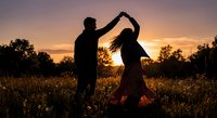 Romantic couple dancing in golden sunset field creating heart shape with arms, silhouetted against warm evening sky for love and relationship concepts.