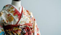 Traditional Japanese kimono with ornate floral and crane patterns in red, gold and white silk fabric, displayed on mannequin against light background.