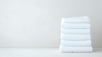Neatly folded stack of fresh white cotton bath towels on light background, minimalist composition for spa, hotel and bathroom interior styling.