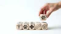 Hand placing wooden cube with paw print among veterinary care symbols on white background for pet health insurance and medical services design.