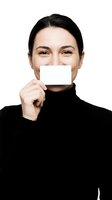Young woman of East Asian descent wearing a black turtleneck holds a blank white card covering her mouth against a white background. Suitable for business, marketing, communication, and advertising campaigns.
