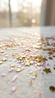 Gold star confetti and pink glitter scattered on white fabric surface with soft bokeh light background, festive celebration decoration.