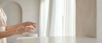 Elegant female hands reaching forward in soft natural light with flowing white curtains creating serene minimalist atmosphere for wellness and beauty concepts.