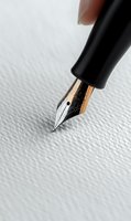 Close-up macro shot of fountain pen gold nib on textured white paper background. Elegant writing instrument ready for calligraphy and creative work.