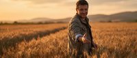Happy male farmer standing in golden wheat field during sunset harvest season with warm lighting and rural landscape background.