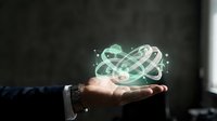 Businessman hand holding glowing atom symbol with orbital electrons, representing science, technology, nuclear energy, and innovation concepts for business and research applications.