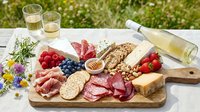 Charcuterie board with cured meats, cheese, nuts, and fresh berries arranged on wooden serving platter outdoors with white wine for entertaining and gatherings.