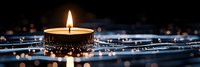 Burning candle with golden flame on dark background with bokeh lights and reflection. Peaceful meditation atmosphere creates serene ambiance.