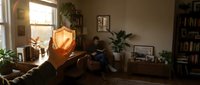 Silhouette of hand holding glowing amber crystal or gemstone in cozy home interior with warm sunlight, plants, and bookshelf for wellness and spirituality concepts.