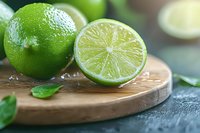 Fresh lime cut in half with water drops on wooden cutting board, close up view with selective focus and natural light for food photography.