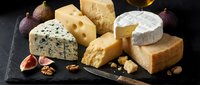 Gourmet cheese platter with blue cheese, brie, aged cheddar and nuts on dark slate board for culinary presentations and food photography.