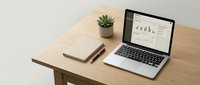 Laptop displaying analytics dashboard on wooden desk with notebook, pen, and potted succulent plant for modern workspace setup.