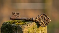 Ornate antique bronze key with decorative handle resting on moss-covered stone surface in natural outdoor setting for vintage design projects.