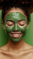 Young African American woman with bright smile wearing green clay facial mask against green background, eyes closed in relaxation and enjoyment of skincare treatment.