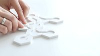 Close-up of hand placing white puzzle pieces together on white surface, symbolizing problem-solving, teamwork, and business strategy solutions.
