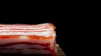 Fresh raw bacon slices with fat layers on dark wooden background, close up view of streaky pork meat cut for cooking and frying.