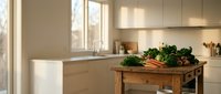 Fresh organic vegetables on a rustic wooden table in a bright modern kitchen with natural light streaming through large windows.