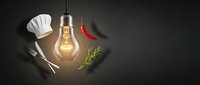 Creative culinary concept with glowing lightbulb surrounded by chef hat, fork, knife, chili pepper and rosemary herb on dark background for cooking inspiration.