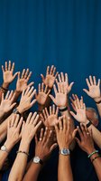 Multiple diverse hands raised up against blue background showing unity teamwork collaboration and volunteer spirit in group setting.