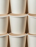 Rows of blank white paper coffee cups arranged in geometric pattern creating minimalist composition with soft beige tones and subtle shadows.