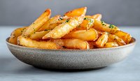 Golden crispy potato wedges seasoned with herbs and spices served in gray ceramic bowl on light background, close up view of homemade comfort food.