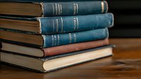 Stack of vintage blue hardcover books with worn spines and aged pages on wooden surface, creating nostalgic academic atmosphere suitable for education and literature themes.