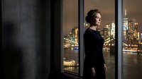 Professional businesswoman in elegant black dress standing by office window overlooking illuminated city skyline at night for corporate lifestyle concepts.