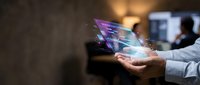 Hands holding transparent digital tablet with holographic interface and glowing data visualization for technology, innovation, and business solutions.