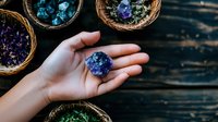 Raw amethyst crystal cluster held in feminine palm surrounded by woven baskets filled with colorful healing stones on dark wooden surface, spiritual wellness concept.