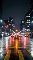 Blurred city street at night with wet asphalt reflecting colorful lights from traffic and buildings creating atmospheric urban bokeh effect.