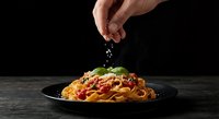 Hand sprinkling cheese over delicious spaghetti pasta with tomato sauce and fresh basil on dark wooden table for culinary presentation.