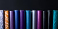Colorful metallic holographic foil rolls arranged in row showing vibrant iridescent surface texture with blue, purple, and silver reflective materials.
