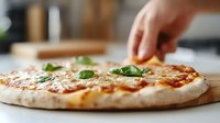 Fresh homemade margherita pizza with melted mozzarella and basil leaves on wooden cutting board, hand reaching to take slice in bright kitchen setting.