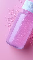 Pink glittery liquid in transparent bottle with scattered pearl beads on pink background, modern minimalist cosmetic product photography styling.